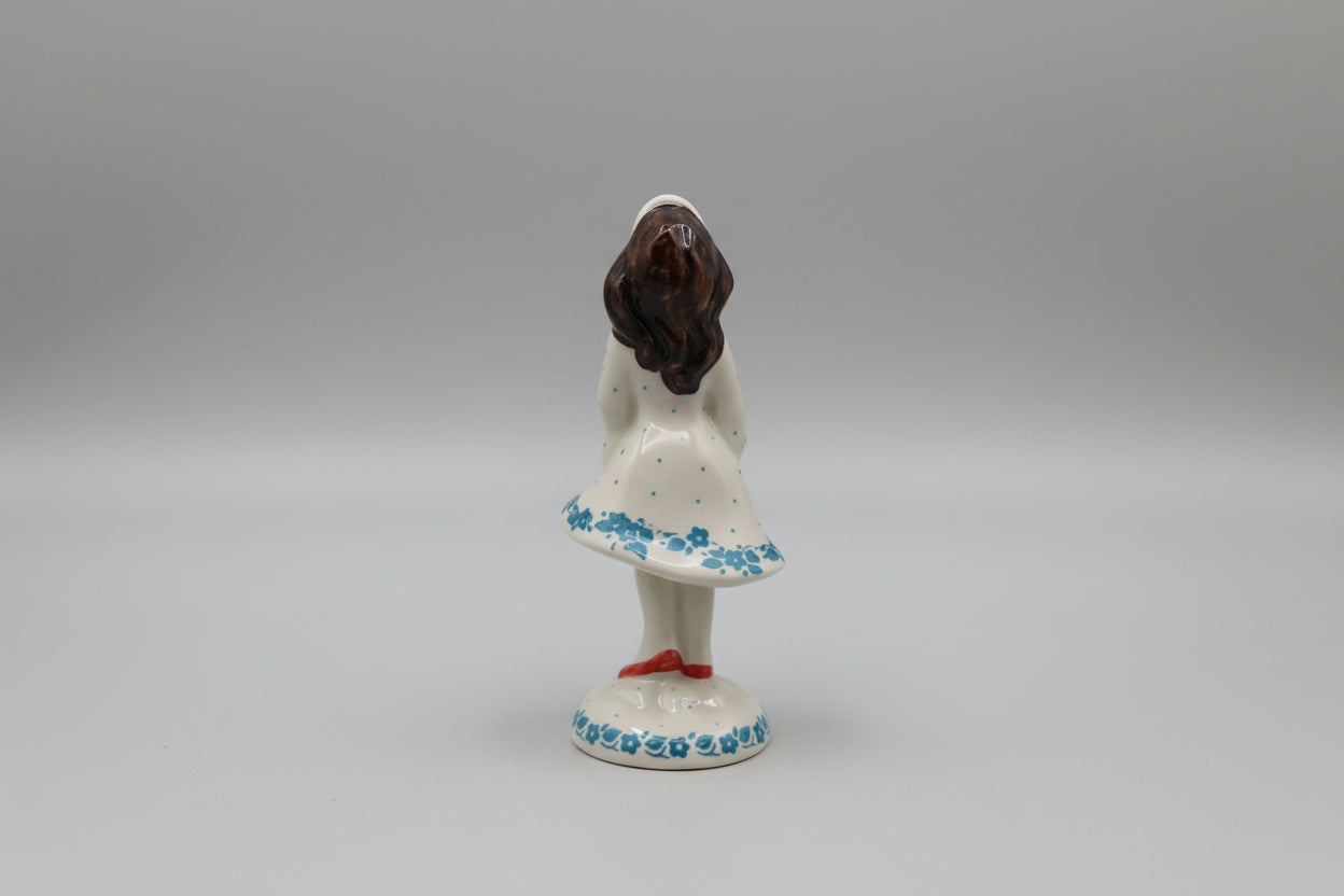 Small figurine of a woman in a white dress with blue floral patterns on a white lace doily.