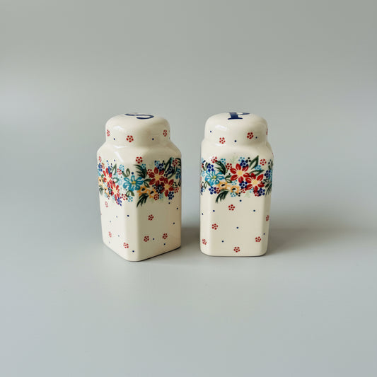 Two ceramic salt and pepper shakers with floral designs on a lace tablecloth.